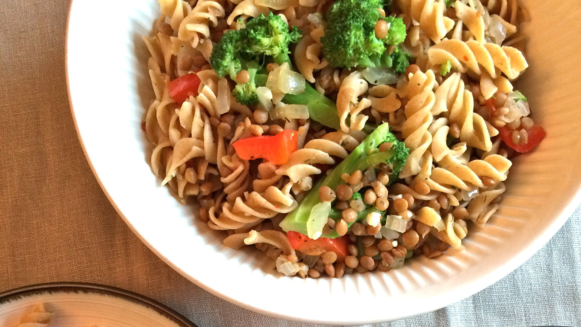 Un grand bol de pâtes au brocoli et aux lentilles, avec deux portions dans des assiettes avec des fourchettes.