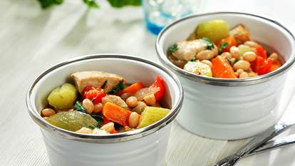 Deux bols blancs remplis de poulet cuit, de carottes, de céleri, de haricots blancs et de bouillon.