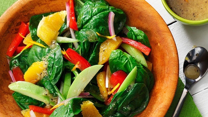 Bol d'épinards avec des segments oranges, poivrons rouges, oignons dans un bol en bois avec vinaigrette