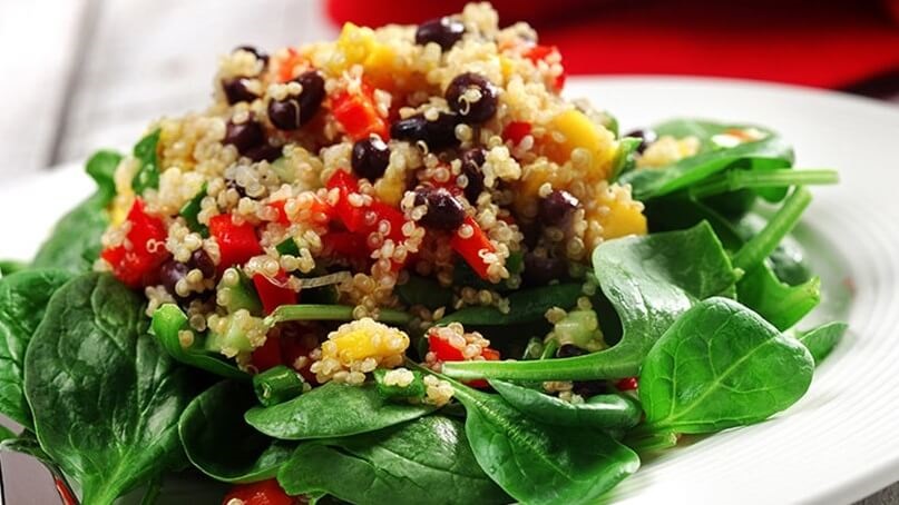 Quinoa cuit, poivron rouge haché, mangue et haricots noirs sur un lit d’épinards