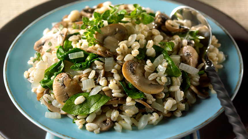 Pilaf d'orge aux épinards et champignons servi sur une assiette bleue avec une cuillère