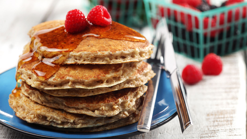 Pile de crêpes garnies de framboises dans une assiette bleue.