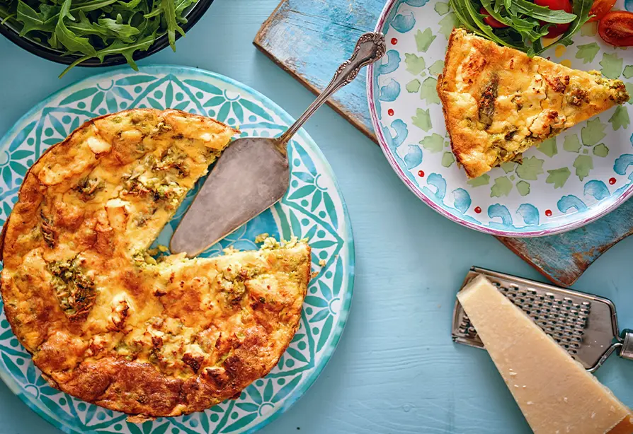 Frittata au saumon dorée avec une pelle à tarte dans une assiette à motifs bleus.