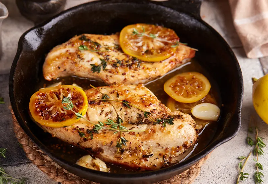 Poitrine de dinde tranchée recouverte de sauce et garnie d’herbes fraîches, dans une poêle en fonte.
