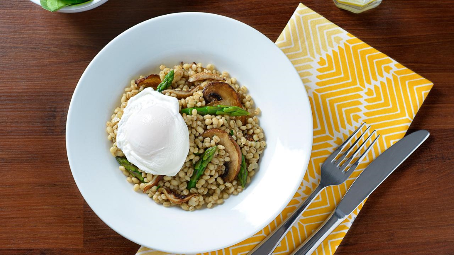 Oeuf poché avec pilaf d'orge aux champignons dans un bol de service blanc sur une serviette à motifs jaunes.