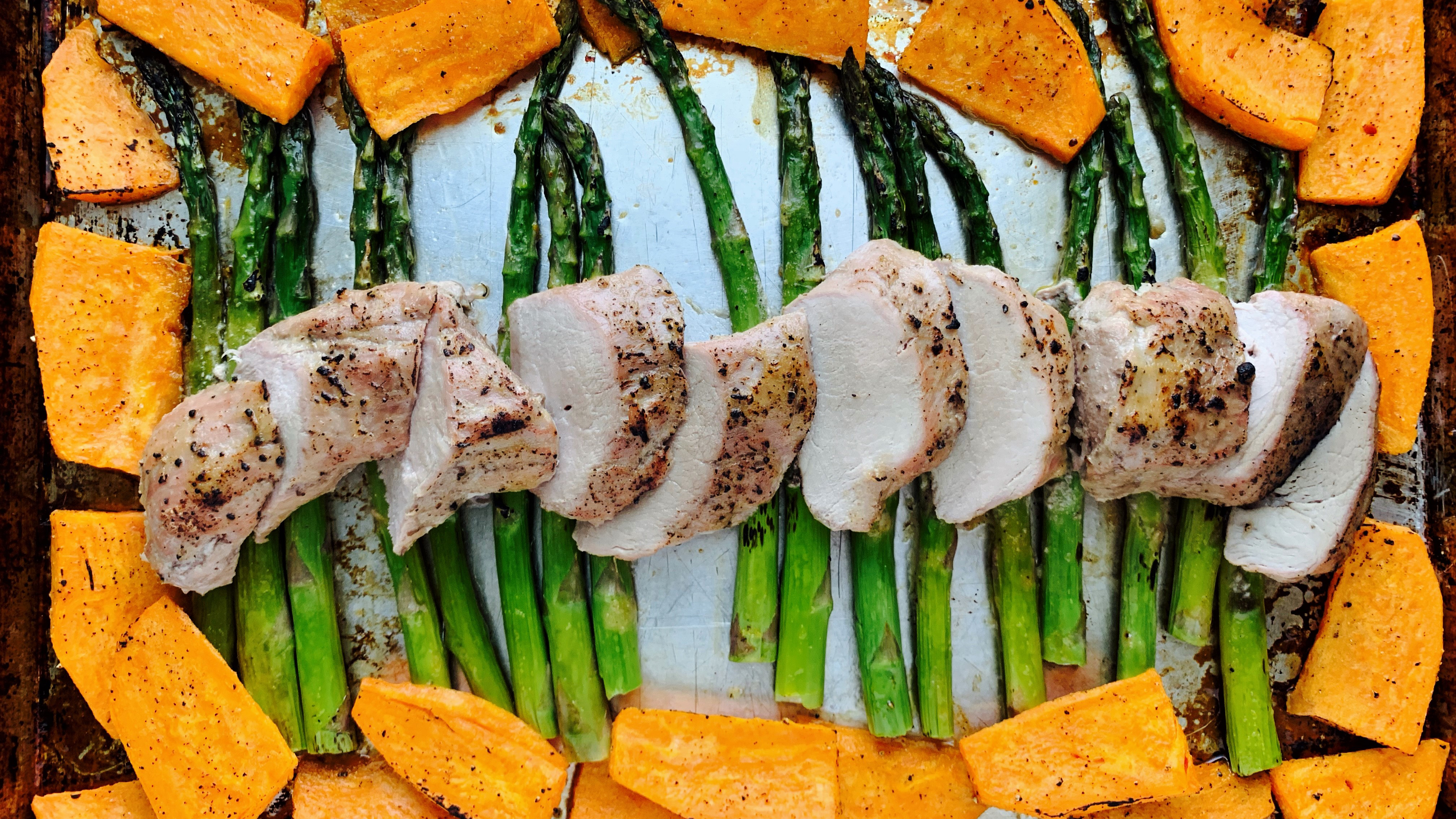 Un filet de porc sur une plaque à cuisson avec patates douces et asperges