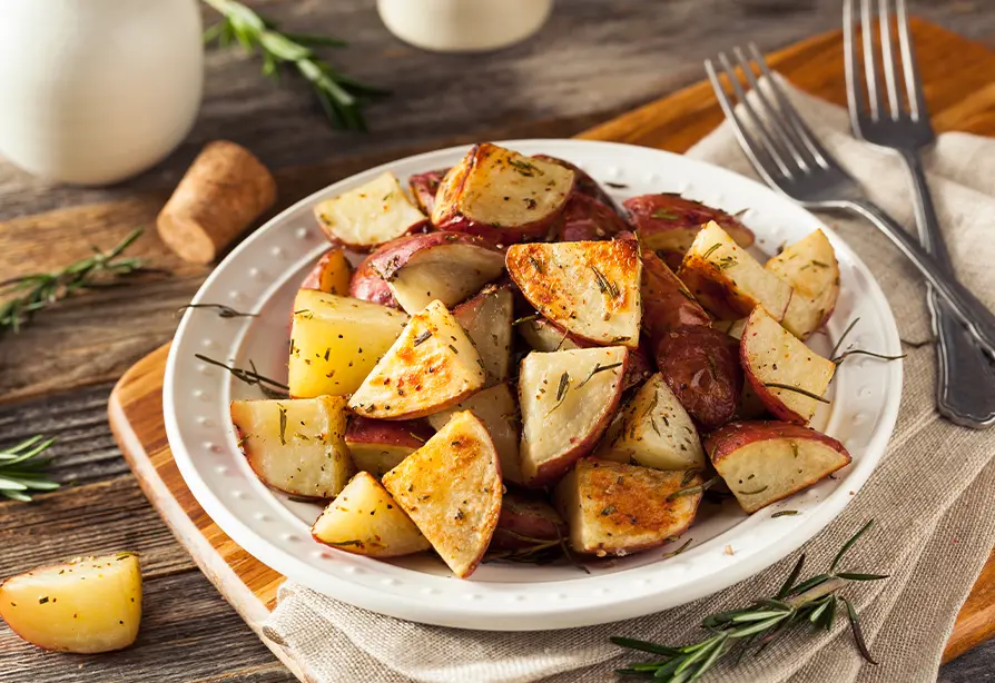 Pommes de terre rôties avec romarin dans une assiette blanche placée sur une planche en bois avec des fourchettes.