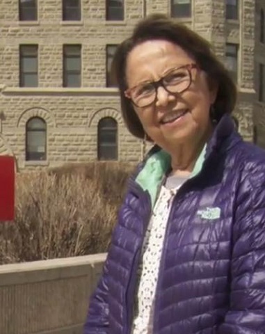Esther Sanderson sourit, habillée d’une veste violette, à côté d’un panneau de l’Université de Winnipeg.