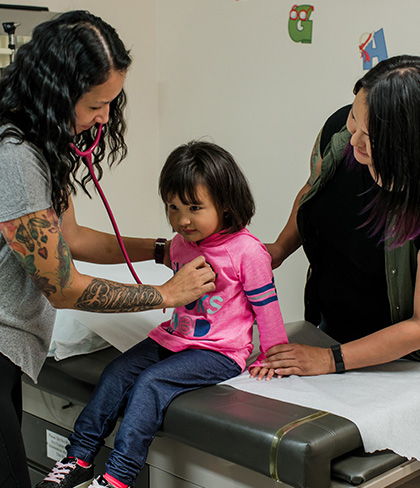 Une médecin examine une fillette avec un stéthoscope pendant que la mère tient la main de l’enfant. 