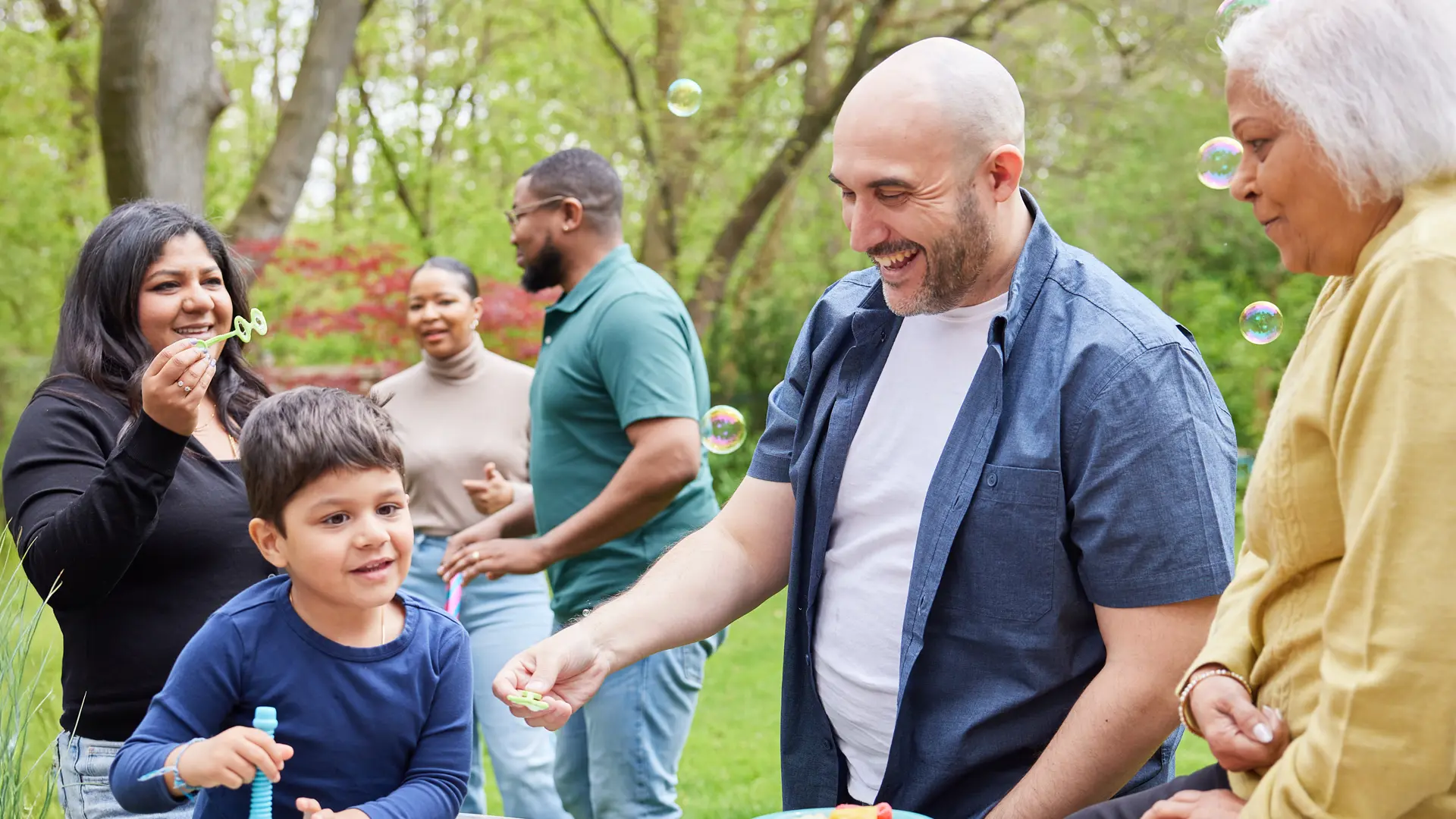 Des adultes soufflent des bulles avec un enfant dans un parc.