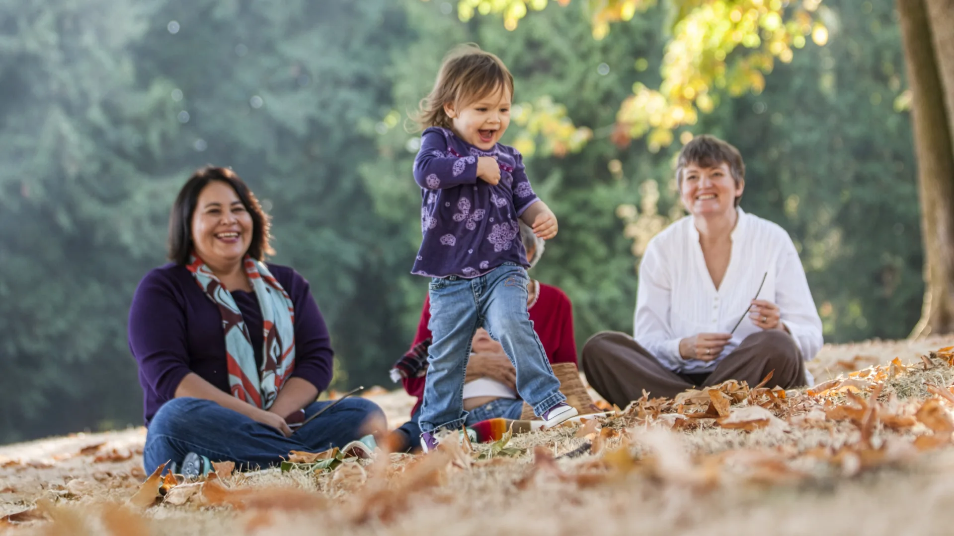 Des personnes assises dans un parc avec une enfant qui joue.