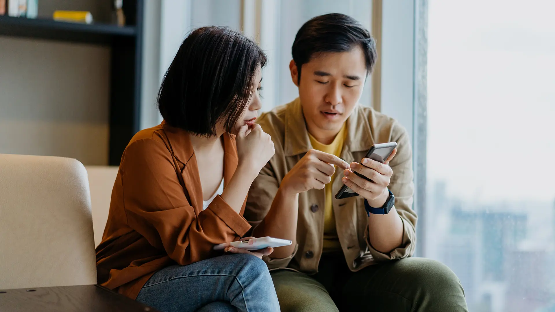 Deux personnes assises sur un divan qui regardent des téléphones intelligents.