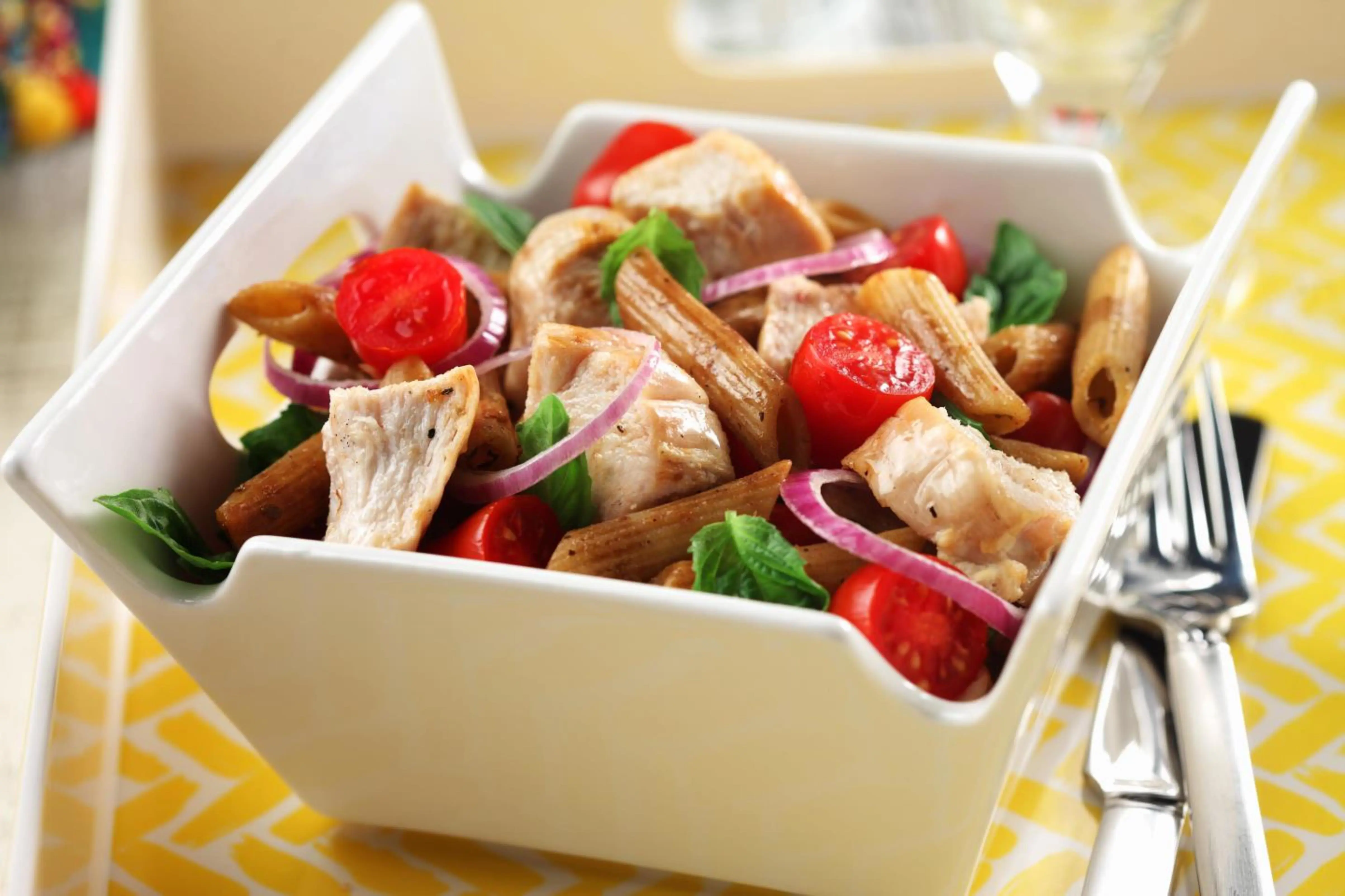 Salade de pâtes au poulet bistro dans un bol carré blanc avec une fourchette sur une nappe jaune
