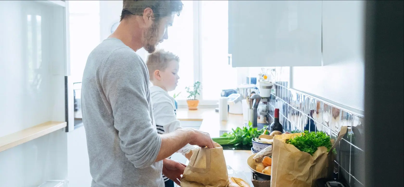 Dans une cuisine, un père et son fils rangent des articles d’épicerie.