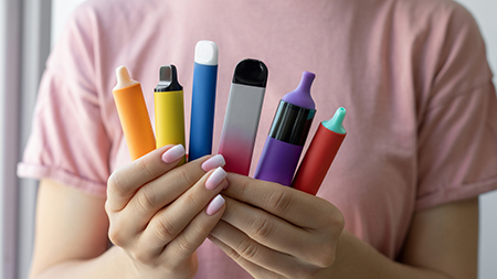 Une personne tient une variété de produits de vapotage déployés en éventail