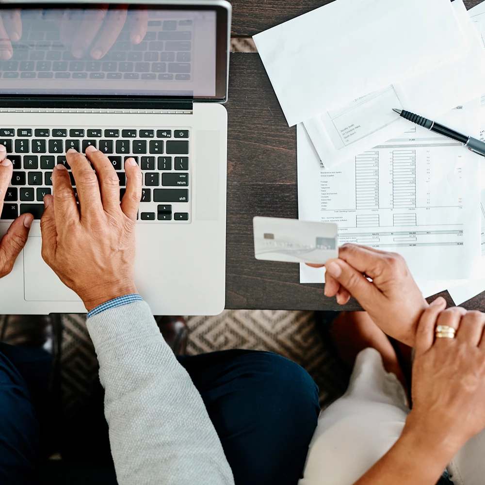 Vue du dessus des mains de deux personnes, l’une qui remplit des documents et l’autre qui utilise un ordinateur portable.