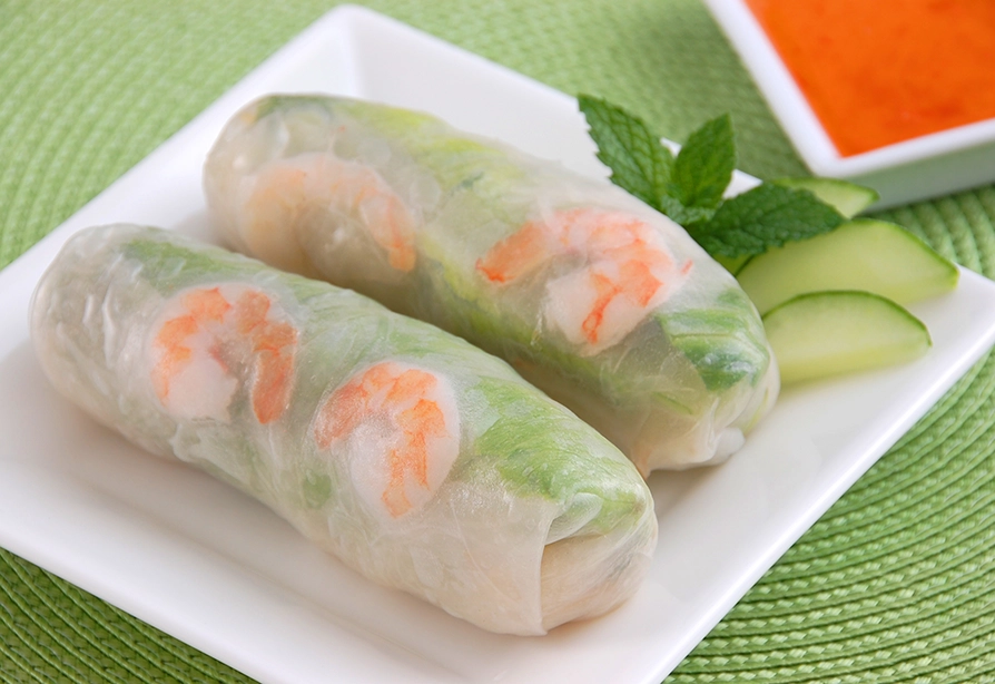 Deux rouleaux printaniers aux crevettes servis sur une assiette blanche avec des tranches de concombres et un brin de menthe.