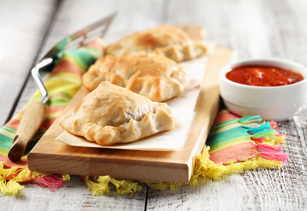 Trois mini calzones sur une planche à découper en bois avec un bol de sauce marinara. 
