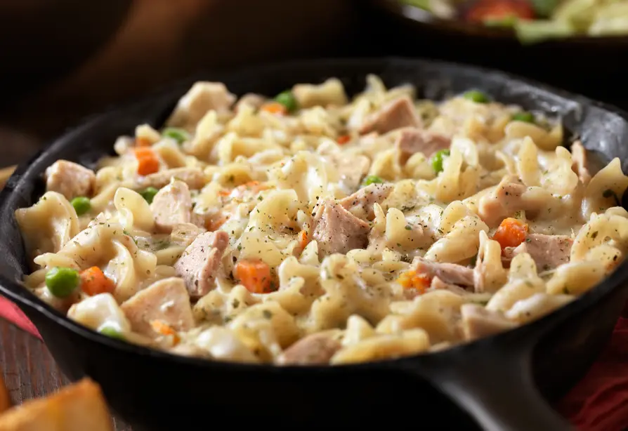 Un plat de pâtes au thon avec des pois verts et des carottes.