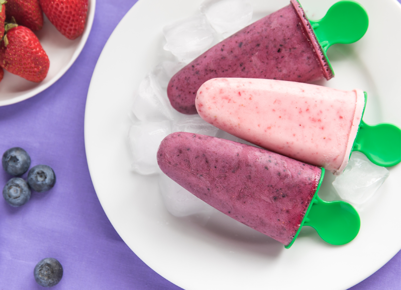 Trois sucettes glacées au yogourt et aux petits fruits dans une assiette blanche. 