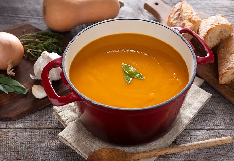 Casserole rouge contenant un potage orange crémeux garni de feuilles vertes. 
