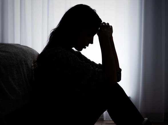 Assise dans une pièce sombre, une femme semble en situation de stress