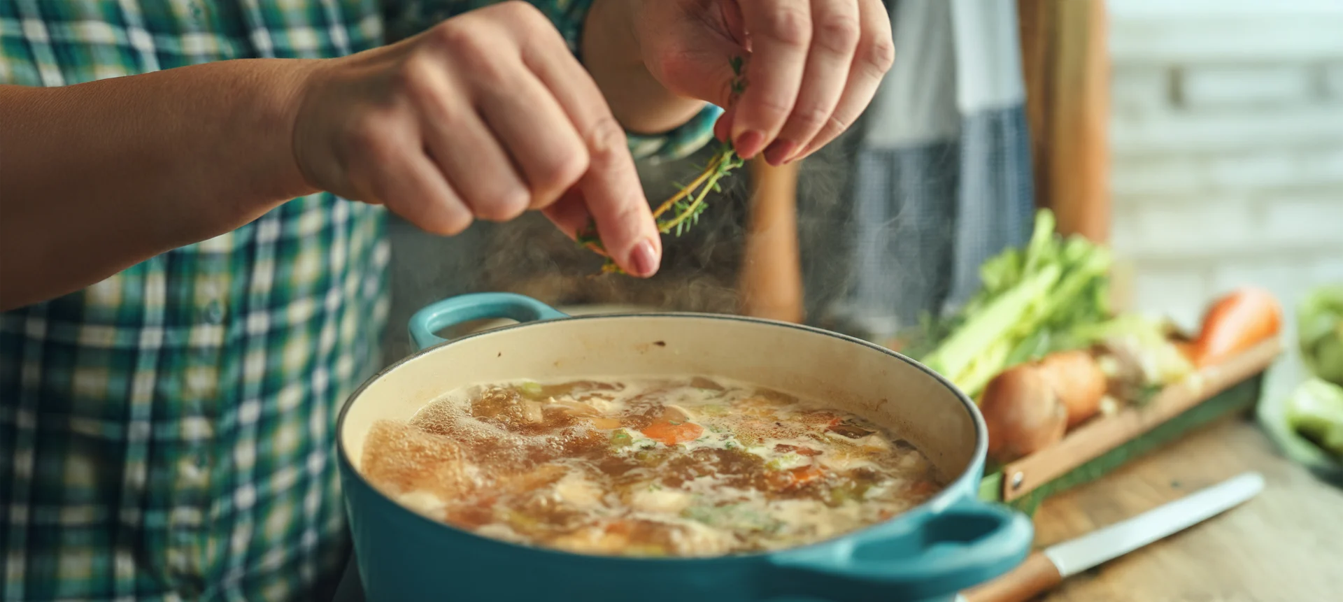 Une femme assaisonne une casserole de soupe maison avec des herbes fraîches.