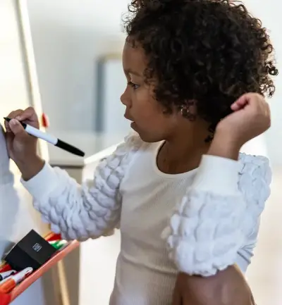 Nora dessine sur son tableau blanc chez elle.