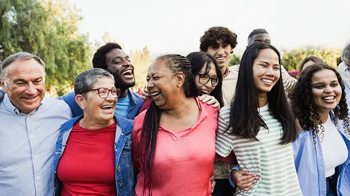 Un grand groupe diversifié de personnes s’enlacent à l’extérieur en souriant.