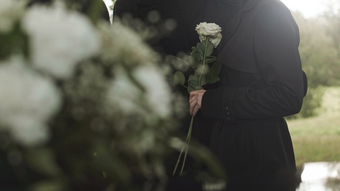 Une personne tient une rose blanche lors d’une cérémonie commémorative en plein air.
