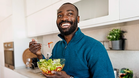 Une personne dans une cuisine tenant un bol de salade et mangeant à la fourchette.