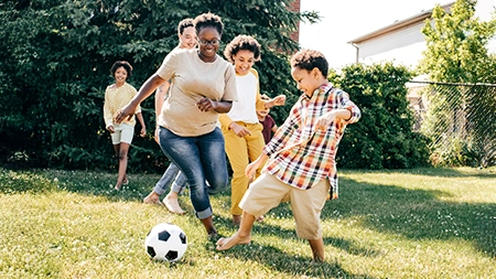 Un groupe d’enfants et d’adultes jouent au soccer ensemble sur une pelouse ensoleillée.