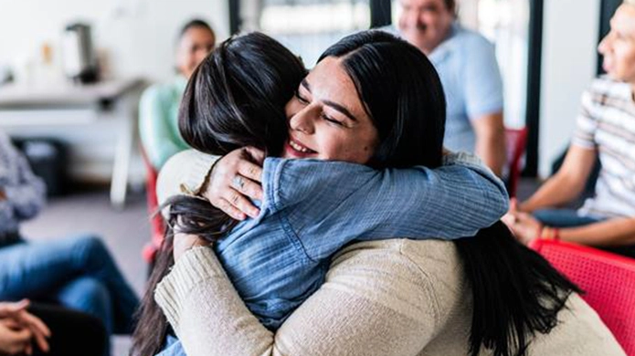 Deux personnes se font une accolade et des gens sont assis en arrière-plan.