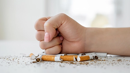 Une main serrée dans un poing sur des cigarettes cassées sur une table.