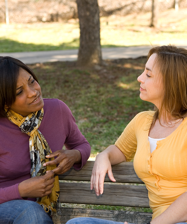 Deux femmes discutent, assises sur un banc à l’extérieur.