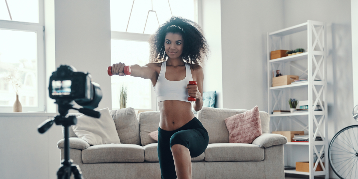 Une femme en tenue de sport s’entraîne avec des poids devant une caméra vidéo