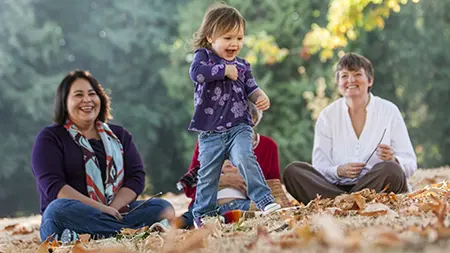 Des personnes assises dans un parc avec une enfant qui joue. 
