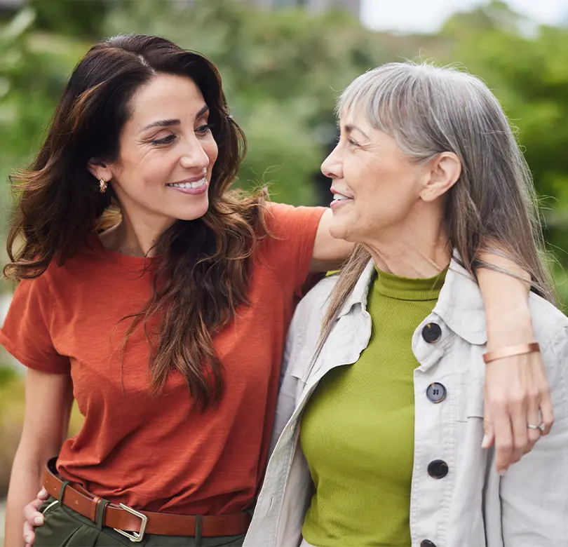 Une jeune femme avec son bras autour d'une femme plus âgée, souriant et marchant ensemble.