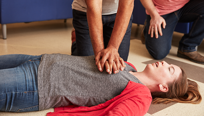 Two people leaning over a woman on the floor, giving her chest compressions.
