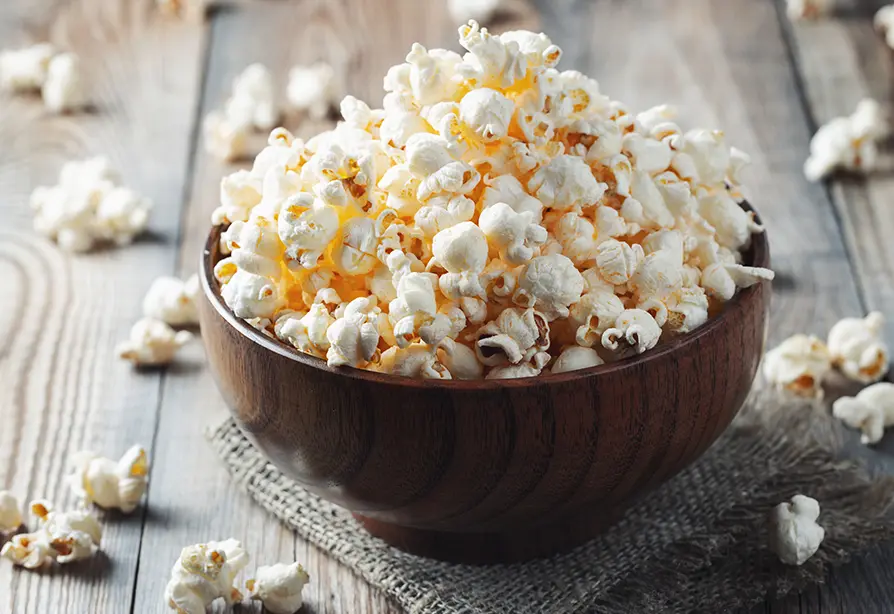 Bol rempli de maïs soufflé sur une table en bois.