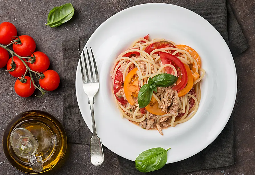 Une assiette de spaghettis et de thon avec poivrons et tomates.