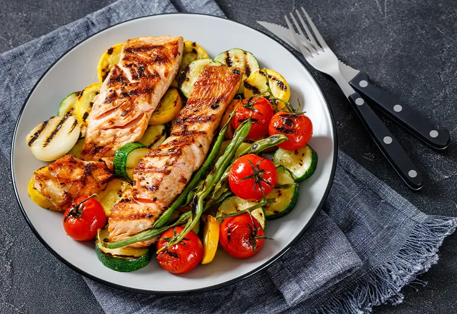 Saumon grillé servi sur un lit de légumes dans une assiette blanche.