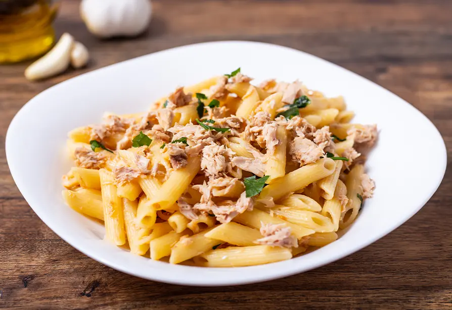 Penne garnis de thon émietté et servis dans un bol blanc.