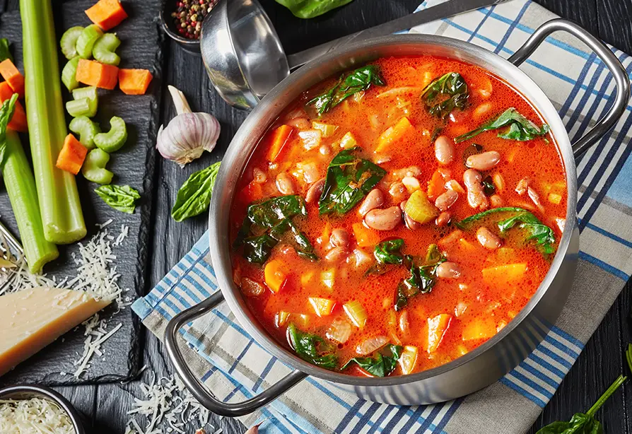 Casserole de soupe aux légumes avec haricots et légumes-feuilles sur un linge à vaisselle carreauté.