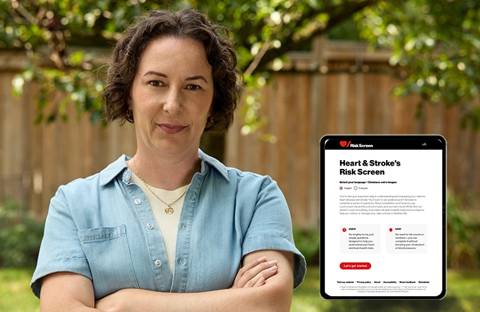 Adria Scarano se tient debout à l’extérieur avec les bras pliés près d’une tablette affichant l’écran de Vérif-Risques de Cœur + AVC.