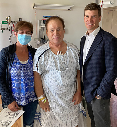 Darrell Parker à côté de son lit d’hôpital, accompagné de sa femme, Shirley Parker (à gauche), et du chirurgien qui lui a sauvé la vie, le Dr Corey Adams (à droite).