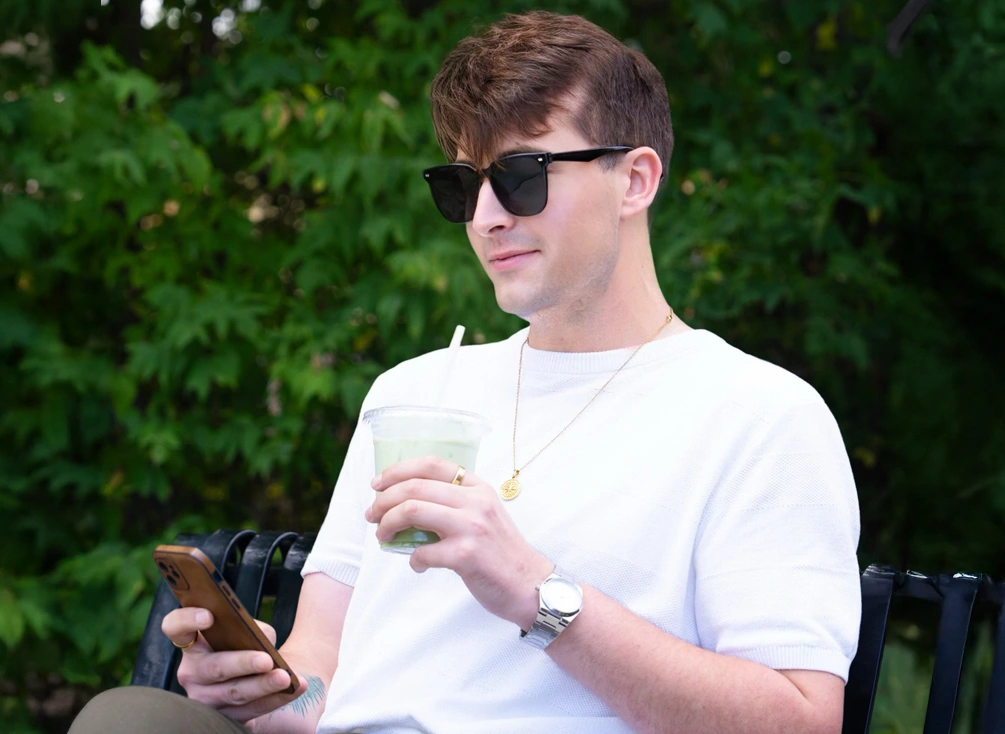 Donald consulte son téléphone en sirotant un jus, assis dehors sur un banc.