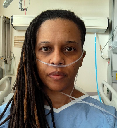 Photo de Katherine Isaac dans une chemise d’hôpital avec un tube à oxygène. 
