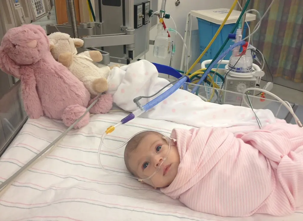 Milana, bébé, enveloppée dans une couverture et couchée dans un lit d’hôpital.