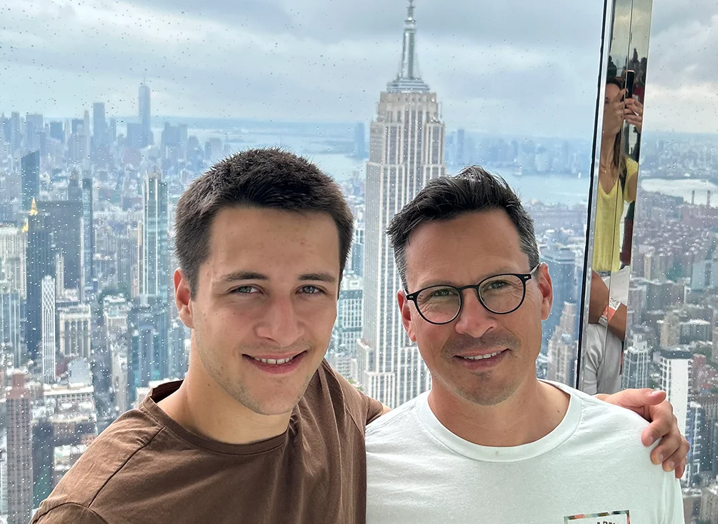 Deux hommes bras dessus, bras dessous, devant l’Empire State Building. 